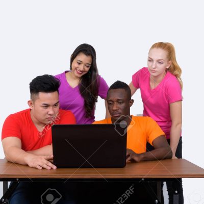 Studio shot of diverse group of multi ethnic friends using laptop on wooden table together with friends watching at the back